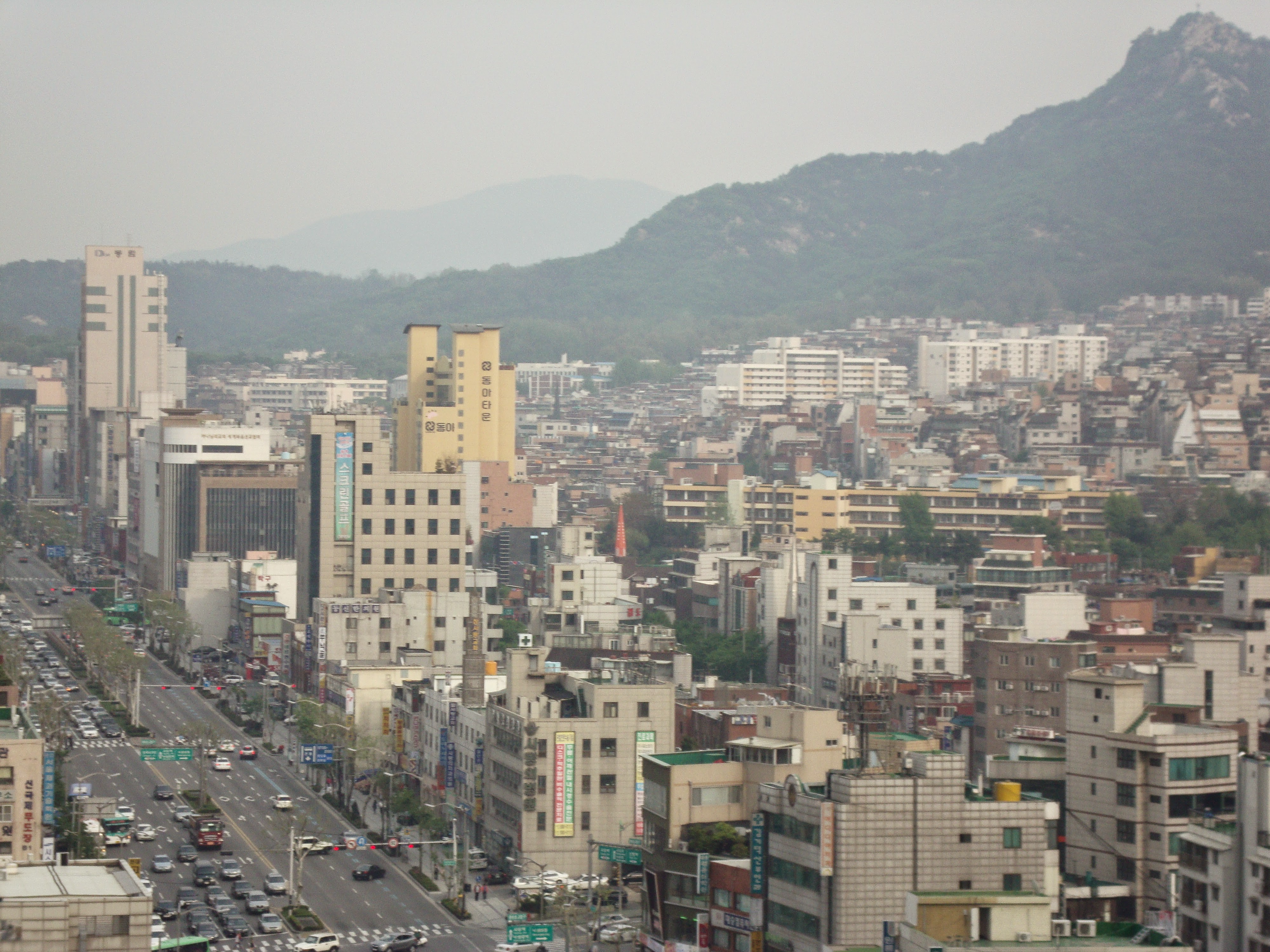 From the roof of the author's apartment building near Seoul National University station, a picture taken in early evening looking southeast on Seoul's sprawl of high rise aparments, businesses lining the roads, and mountains in the distance.