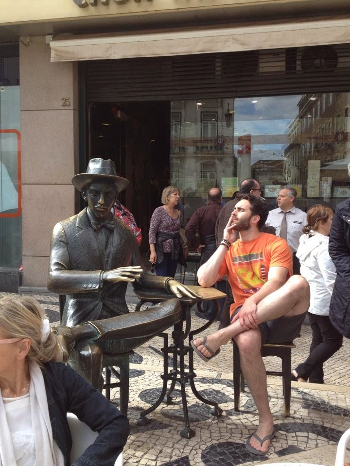 The author sitting at a table with a statue of Fernando Pessoa in Lisbon